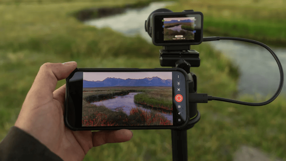 Смартфон, подключённый кабелем к камере GoPro MISSION 1 PRO на штативе, для проводного предварительного просмотра изображения