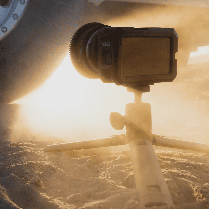 Камера GoPro MISSION 1 PRO на мини-штативе во время съёмки в песчаной пустыне на фоне колеса внедорожника